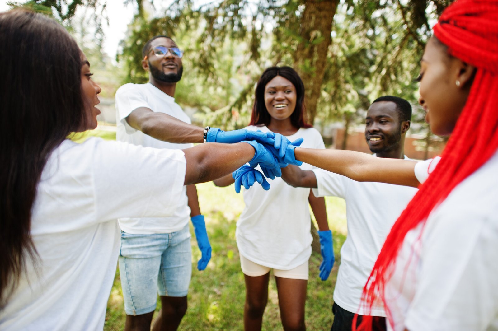 group of happy african volunteers put hands in hands in park. af