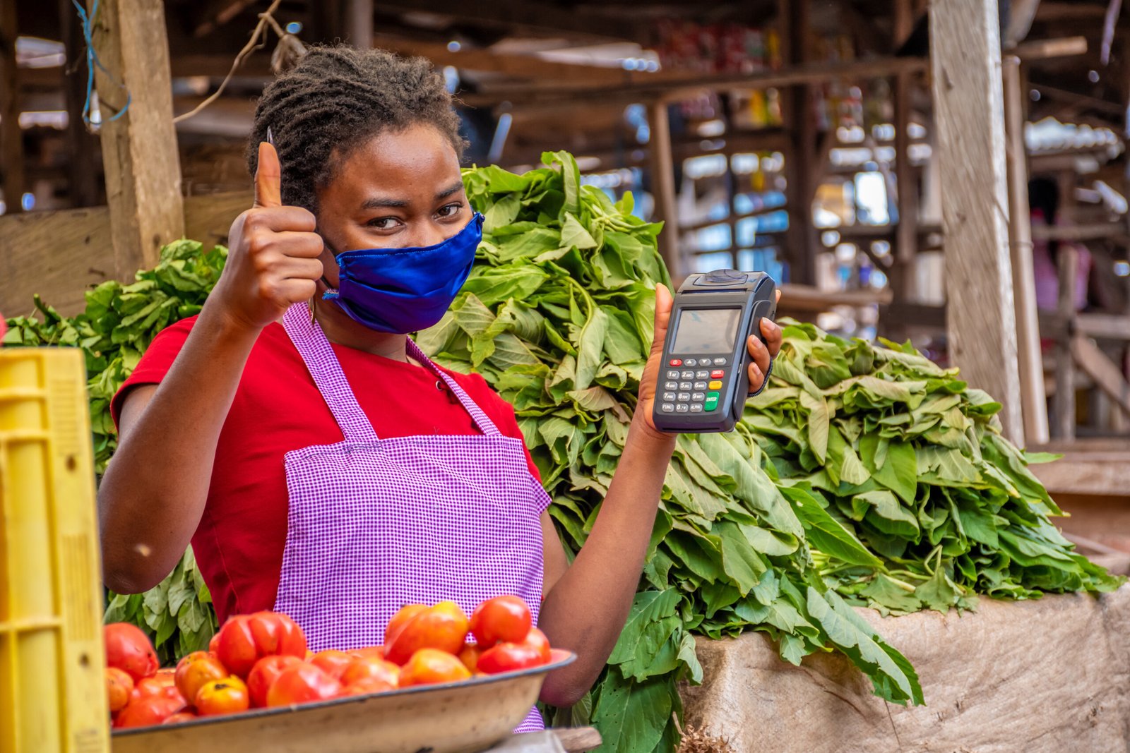 shallow focus of an african female with a facemask holding a pos machine at a market